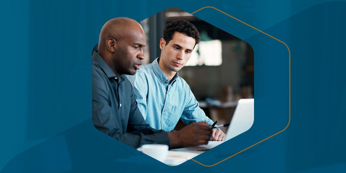 Two men in button up shirts work on a laptop